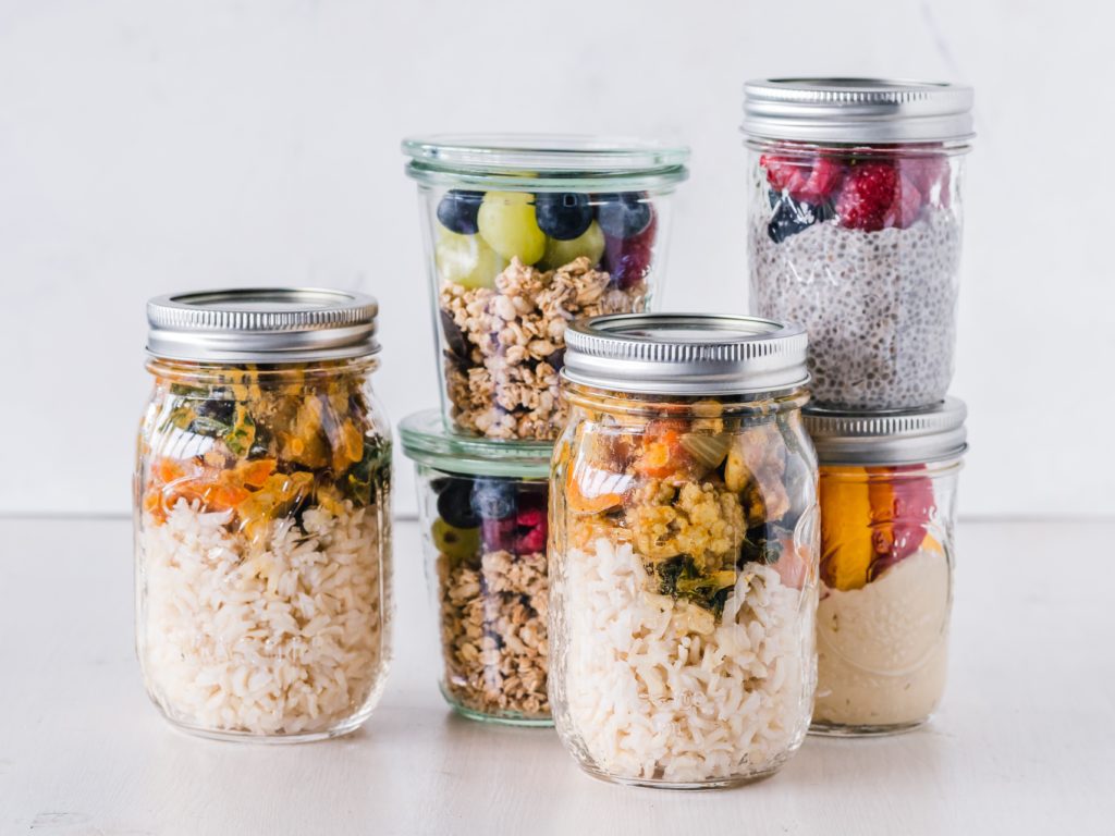 Food prepared in jars: curry and rice, granola and fruit, hummus and crudités, chia pudding and fruit